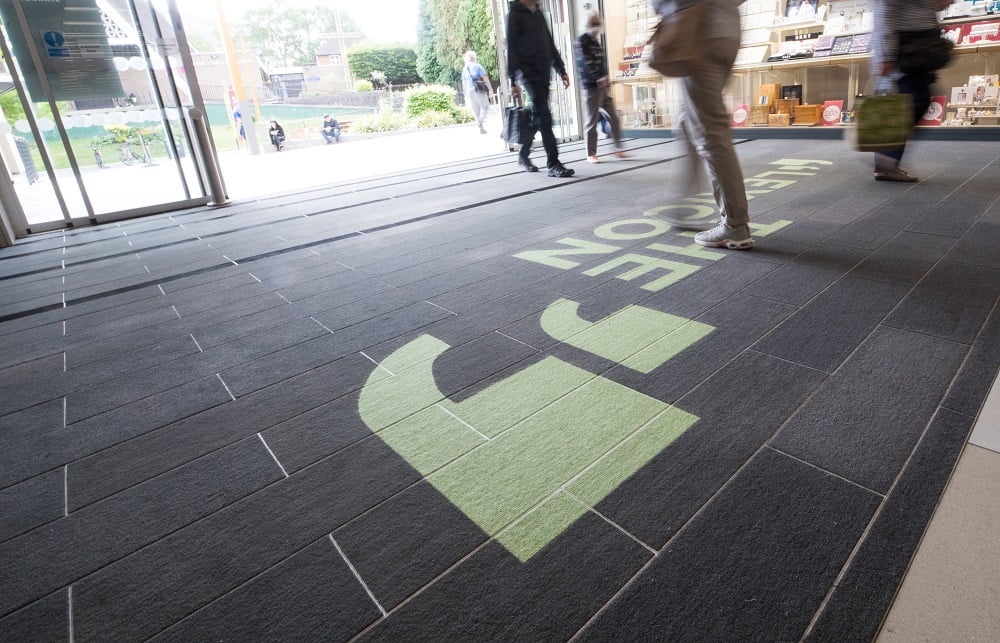 shoppers walking over entrance mattign inset with The Lexicon logo in green
